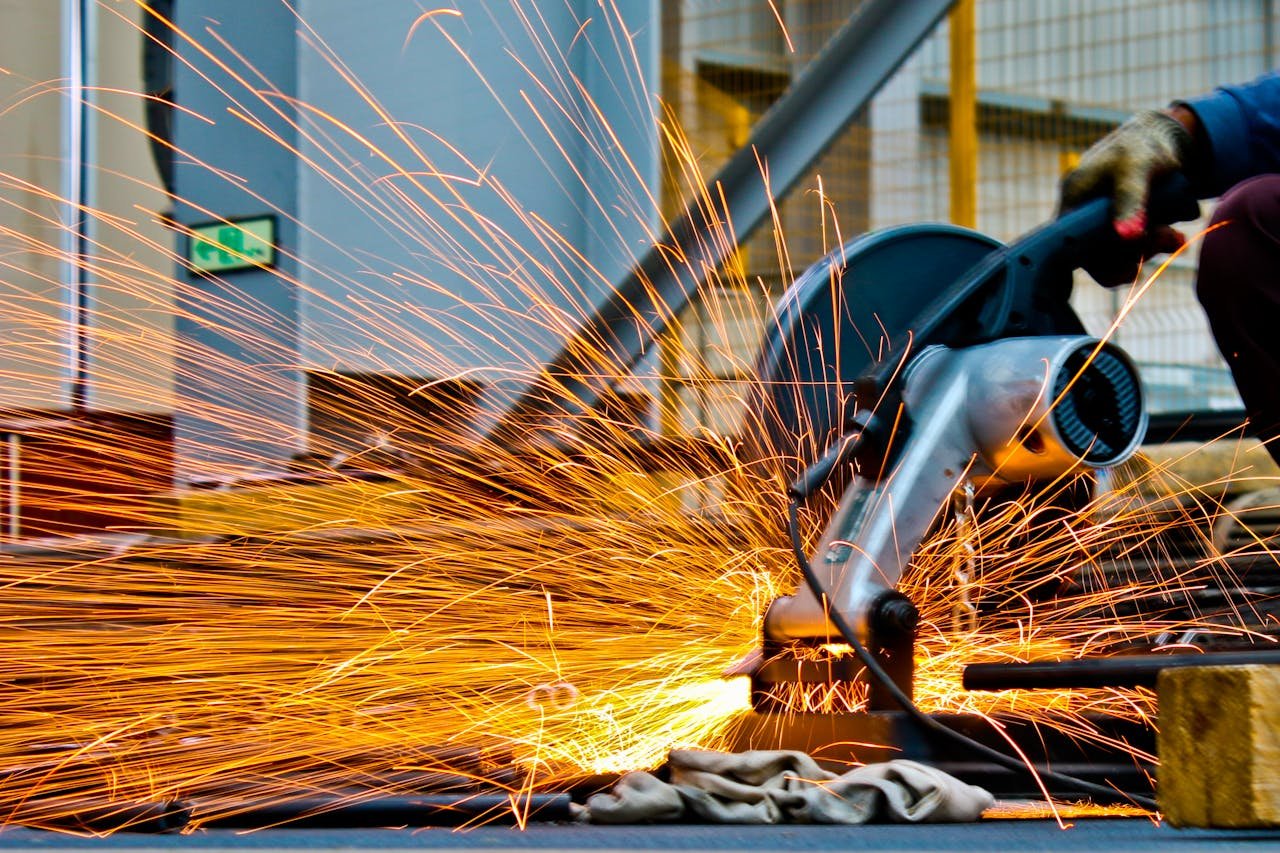 services-03 A worker operates a grinder cutting metal, creating a vibrant display of sparks in an industrial setting.
