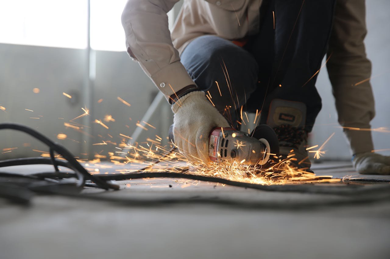services-02 A skilled industrial worker uses a grinder creating a burst of sparks indoors.