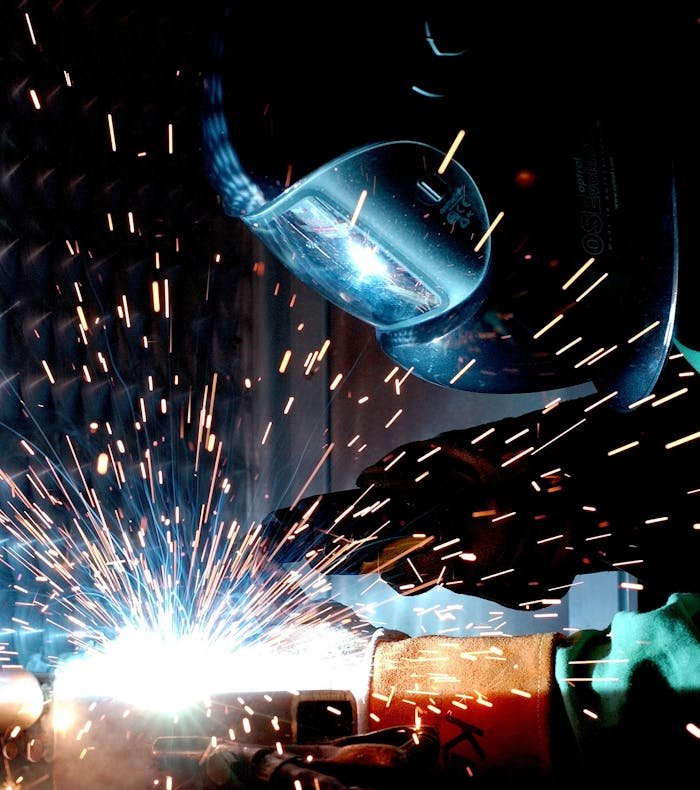 why-choose-us A focused welder works with metal in an industrial setting, creating vibrant sparks.